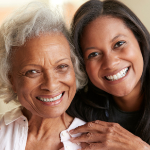 Portrait Of Senior Mother Being Hugged By Adult Daughter At Home