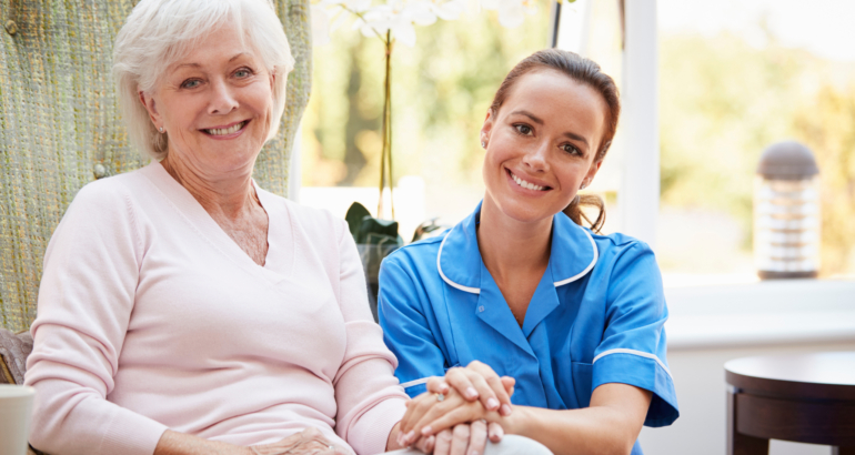 Portrait Of Senior Woman Sitting In Chair With Nurse In Retirement Home